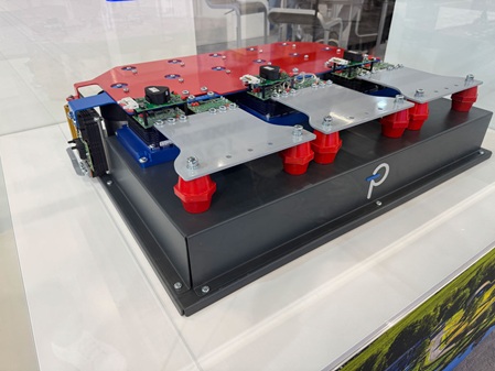 Foto zeigt ein Display auf einem Messestand. Auf einer abgekanteten und pulverbeschichteten Haube wurden mehrere Elektronikbauteile aufgeschraubt. Vorne an der Haube ist ein mehrfarbiges Logo aus Acrylglas intarsial eingelassen. Das Logo wird mit LED-beleuchtet.
