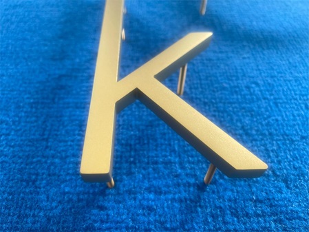 gelaserter 10 mm Edelstahlbuchstabe, Oberfläche und Kanten geschliffen und glasperlgestrahlt, rückseitig geschweißte Stehbolzen. Nachträglich TiN-beschichtet