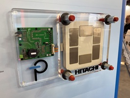 Acrylglassockel aus farblosem Material mit mehreren Bohrungen, Gewinden, und umlaufender Fase. Auf dem Sockel wurden mehrere Elektronikbauteile als Display für einen Messestand verschraubt. Auf dem Sockel sind zwei Firmennamen mit buntem Acrylglas in Taschen eingelassen und verklebt worden. Dieser Sockel wurde an einer Wand eines Messestands befestigt.
