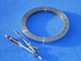 Foto zeigt einen Zahnkranz aus Edelstahl mit einer Laserbeschriftung. Die Beschriftung zeigt die Zahlen 00 bis 23. Als Größenvergleich liegt ein Zirkel neben dem Zahnkranz. Beide liegen auf einem blauen Hintergrund. Der Zahnkranz ist Teil einer Sonnenuhr.