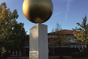 Metallkugel, goldfarbig glänzend lackiert, auf Granitstele. Graviertes Edelstahlschild.